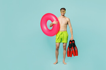 Full body young fun sexy man wear green shorts swimsuit relax near hotel pool hold in hand inflatable rubber ring flippers isolated on plain blue background. Summer vacation sea rest sun tan concept. © ViDi Studio