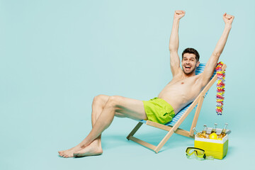 Full body overjoyed happy young sexy man wear green shorts swimsuit relax near hotel pool sit in...