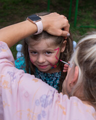 .The girl draws a picture on the face of a little girl..The face of a little girl with a pattern on...
