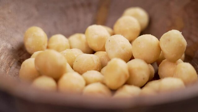 Shelled macadamia nuts falling into a wooden bowl in slow motion. Nutritious natural food. Close up