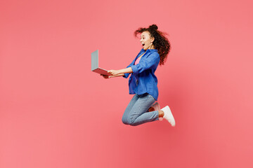 Full bocy side view young IT woman of African American ethnicity she wear blue shirt casual clothes jump high hold use work on laptop pc computer isolated on plain pink background. Lifestyle concept.