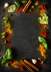 Spices and herbs on black slate background. Pepper, turmelic, dill, cinnamon, basil, rosemary, chilly, cardamom. Top view with copy space.