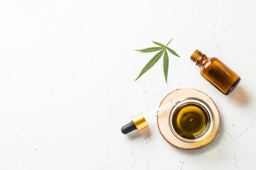 CBD oil and cannabis leaves at white table. Medicine and cosmetic product. Flat lay image with copy space.