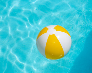 Beach ball, yellow and white, floating in cool blue pool water.