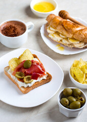 Sandwich with jamon and olives, decorated with chips, also a croissant with cream cheese and honey, a cup of coffee. European breakfast option.
