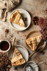 Three plates with traditional apple pie pieces served for an autumn cozy tea party. Rustic stil life, brown textured background. Autumn seasonal food concept, top view