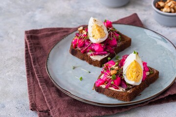 Open sandwiches on rye bread with beetroot salad, boiled egg and microgreens on a ceramic plate on a gray concrete background. Swedish cuisine.