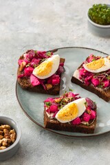 Open sandwiches on rye bread with beetroot salad, boiled egg and microgreens on a ceramic plate on a gray concrete background. Swedish cuisine.