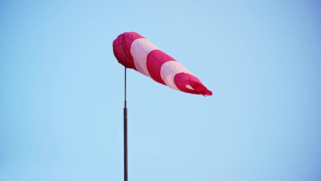 Striped White and Red Windsock Wind Cone Wind Sleeve Indicator Installed on Roof of General Aviation Airport Building Showing Wind Speed and Direction To Pilot Operating Airplane