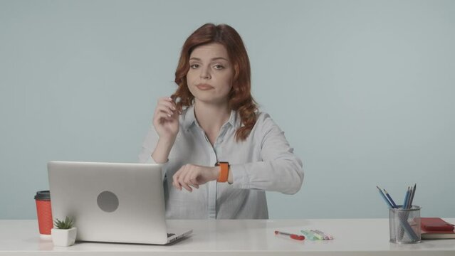 Medium isolated video of a young woman pointing at her watch and negatively wagging her finger to show her complaint about overworking. HDR BT2020 HLG Material.