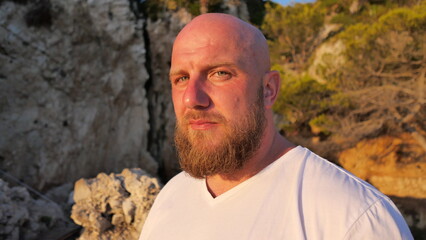 Striking portrait of a man with blue eyes and a beard, set against the picturesque landscape of Cap d'Antibes, France. His tattoos tell a story, embodying a blend of rugged charm and natural beauty