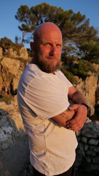 Striking portrait of a man with blue eyes and a beard, set against the picturesque landscape of Cap d'Antibes, France. His tattoos tell a story, embodying a blend of rugged charm and natural beauty