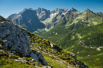 Mountain landscape, where the High Tatras meet the Belianske Tatras, bathed in sunlight and surrounded by emerald-green meadows