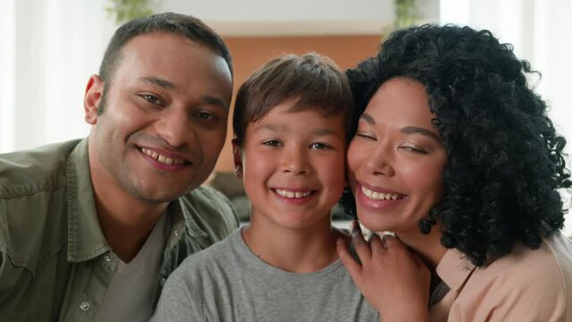 Happy multiracial African American loving mum and dad kissing little boy in cheeks adoption child care family bonding caring parents hug cuddle embrace little kid son love relationship affectionate