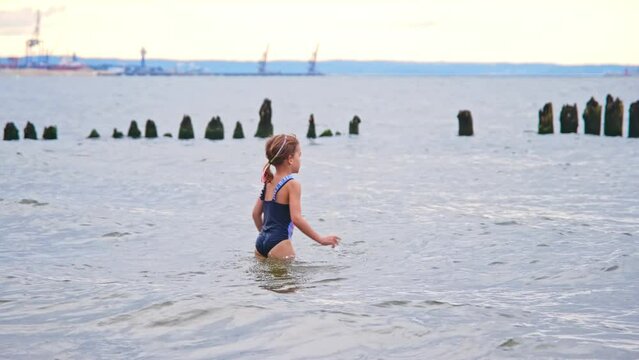 Unsupervised Young Caucasian Girl in Swimsuit Walking into Sea Water Playing with Breaking Waves