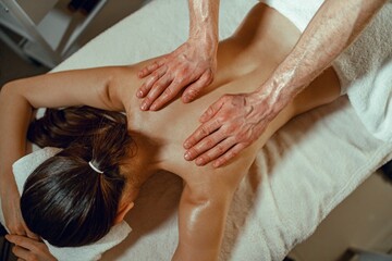 Fototapeta na wymiar Top view masseur man doing back massage using oil to a woman in spa salon. Therapy, resort