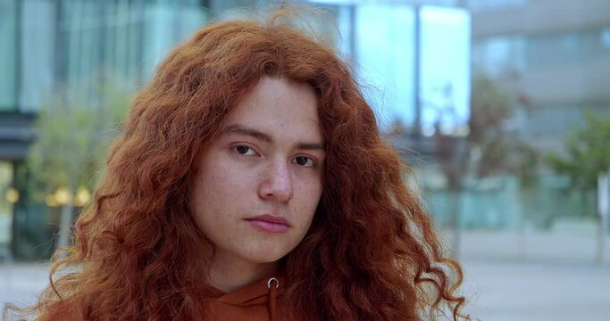 Portrait of a young non-binary person looking at camera seriously in a city. Portrait red-haired person with freckles