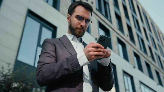 Caucasian tired man using mobile phone in city overworked businessman male ceo business entrepreneur browsing mobile phone internet complete work near office exhausted guy upset with problem outdoors