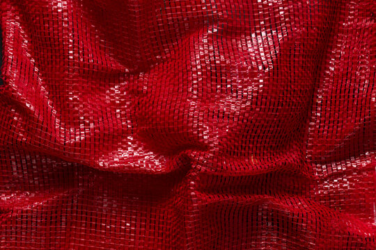 Red woven plastic net for packaging fruits, vegetables, or products. Abstract close-up background. Expanded polyethylene texture.
