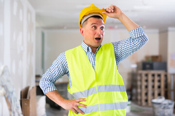 Portrait of surprised man builder. Amazed repairman in yellow vest and hardhat in apartment during...