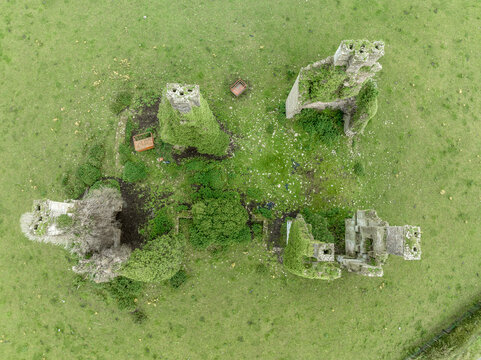 Aerial view of Castlecuffe castle in Ireland, ruined tower house with chunks of corner walls with stone chimneys standing on a green meadow 