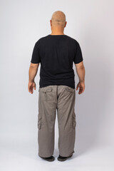 Fototapeta premium Grey-haired man in a black T-shirt and gray pants, rear view, on a gray background.