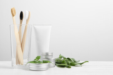 Toothbrushes, dental products and herbs on white wooden table. Space for text