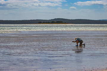 Woman kneeling and photographing a beach at low tide in Eastern Australia.