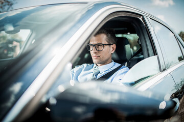 Young caucasian businessman driving a car to work - obrazy, fototapety, plakaty