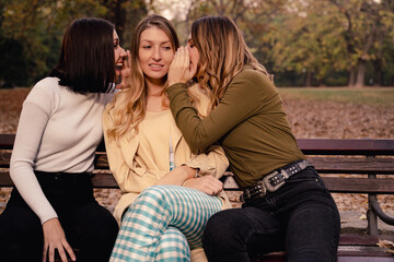 Three girls in the park, sitting on bench and gossiping 