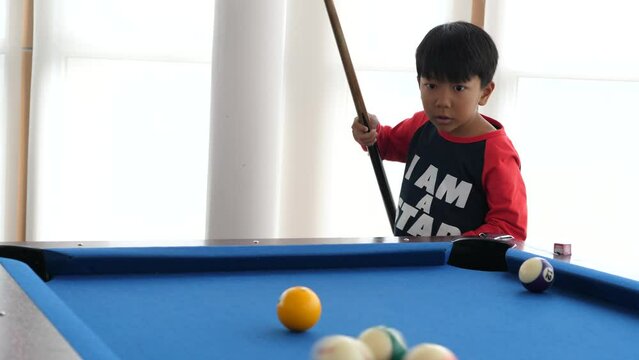 Asian child boy playing billiard or snooker with smiling face, funny shot in the end. Concept of family sport game, leaning, leisure.