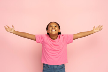 Smiling Nigerian girl in stylish pink t shirt with open arms looking up isolated on pink background