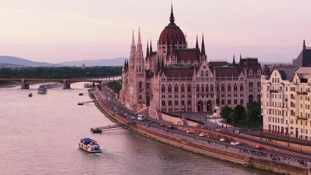 Aerial slide and pan footage of Orszaghaz on Danube riverbank at twilight. Famous travel destination and tourist sight in neogothic style. Budapest, Hungary