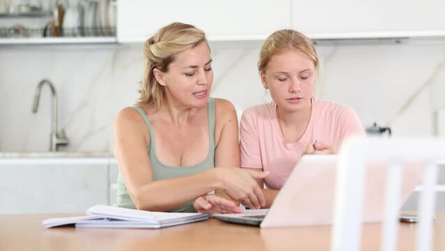 Mom helps her teenage daughter to do her homework and looks carefully at childs notebook. Female tutor performs difficult educational task with child.