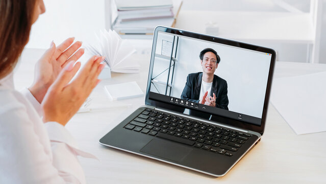 Video congratulations. Distance partnership. Business man on laptop screen and woman colleague celebrating greeting with successful project applauding at workplace.