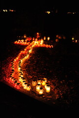 Candle lights on graves and tombstones in cemetery at night in Poland on All Saints’ Day or All...