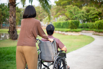 Caregiver take care to elderly woman sitting on wheelchair at public park,Senior health care insurance concept