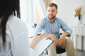 Portrait of female psychiatrist interviewing handicapped man during therapy session, copy space. - obrazy, fototapety, plakaty