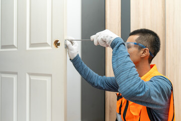 Asian professional locksmith installing or repairing a door knob with screw drive or cordless drill. - obrazy, fototapety, plakaty