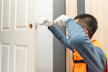 Asian professional locksmith installing or repairing a door knob with screw drive or cordless drill.