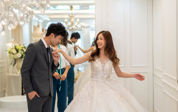 Portrait of smiling happy love asian couple fashion groom man and bride woman talk and try on wedding dress with woman shop owner for pre wedding at wedding interior fashion studio