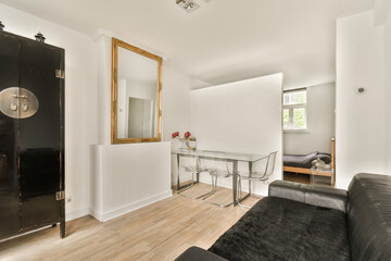 a living room with white walls and hardwood flooring the room has a black leather couch, a glass dining table