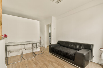 a living room with white walls and hardwood flooring, including a black leather couch in the center of the room