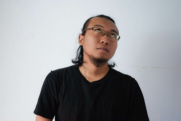 Adult Asian man wearing black t-shirt and eyeglasses with long hair Showing thinking face in grey background.