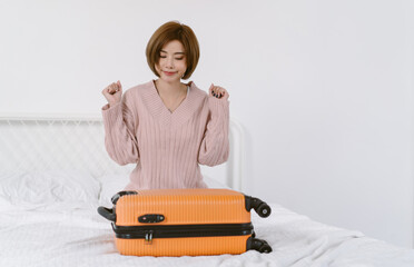Portrait of young Asian woman packing to her clothes into suitcase bag preparing for travel summer trip on bed. Korean or Japanese girl packing traveler case for vacation holiday. Travelling vacation.