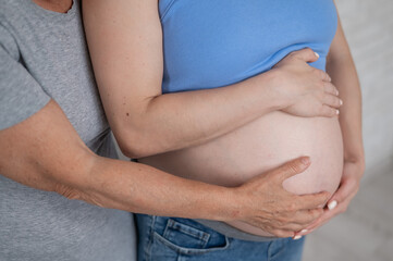 An elderly woman touches the belly of her pregnant daughter. Close-up.