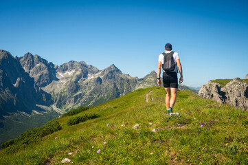 In the heart of the Belianske Tatras, a young hiker embarks on an unforgettable journey along the verdant crest, with the awe-inspiring High Tatras as a backdrop