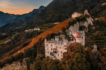 Merano, Italy - Aerial view of the famous Castle Brunnenburg with Tyrol Castle at background in the Italian Dolomites and colorful sunset sky at autumn afternoon