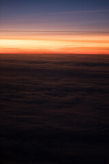 A warm, golden sunset as seen in an aerial view from a passenger airplane flying high above the clouds. The clouds reflect the striking light of the sunset.