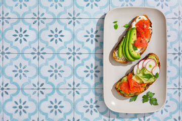 Toast with salmon, avocado and herbs on a rectangular platter. Breakfast concept. Tiled background, hard light.